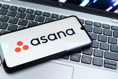 Prag, Çek Cumhuriyeti - 08 01 2025: Dizüstü bilgisayarın üzerinde duran bir cep telefonu Asana logosunu gösterir. Asana görev yönetimi ve takım işbirliği için bir platformdur..