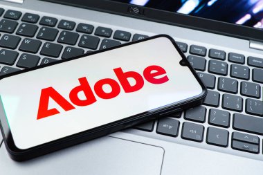 Prag, Çek Cumhuriyeti - 08 01 2025: Dizüstü bilgisayarın üzerinde duran bir cep telefonu Adobe logosunu gösterir. Adobe yaratıcı araçlar ve hizmetler sunan bir yazılım şirketidir..