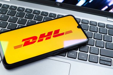 Prag, Çek Cumhuriyeti - 08 01 2025: Dizüstü bilgisayarın üzerinde duran bir cep telefonu DHL logosunu gösterir. DHL uluslararası nakliye hizmeti sunan bir lojistik şirketidir..