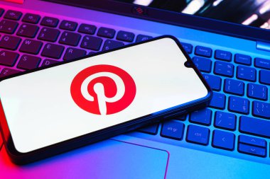 Prag, Çek Cumhuriyeti - 08 01 2025: Dizüstü bilgisayarın üzerinde duran bir cep telefonu Pinterest logosunu gösteriyor. Pinterest fikirleri görsel olarak keşfetmek ve kaydetmek için bir platformdur..