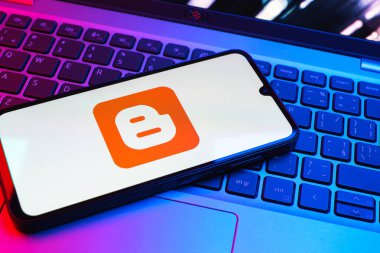 Prag, Çek Cumhuriyeti - 08 01 2025: Dizüstü bilgisayarın üzerinde duran bir cep telefonu Blogger logosunu gösterir. Blogger blog oluşturma ve yayınlama için bir platformdur.