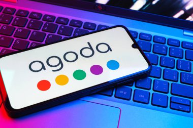 Prag, Çek Cumhuriyeti - 08 01 2025: Dizüstü bilgisayarın üzerinde duran bir cep telefonu Agoda logosunu gösteriyor. Agoda, otelleri ve seyahat yerlerini ayırtmak için bir platform..