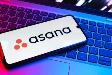 Prag, Çek Cumhuriyeti - 08 01 2025: Dizüstü bilgisayarın üzerinde duran bir cep telefonu Asana logosunu gösterir. Asana görev yönetimi ve takım işbirliği için bir platformdur..