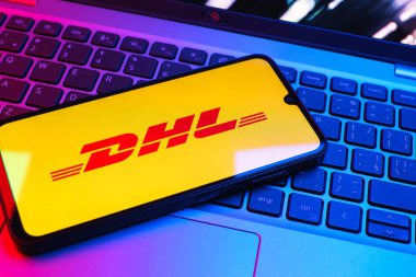 Prag, Çek Cumhuriyeti - 08 01 2025: Dizüstü bilgisayarın üzerinde duran bir cep telefonu DHL logosunu gösterir. DHL uluslararası nakliye hizmeti sunan bir lojistik şirketidir..