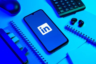 Prag, Çek Cumhuriyeti - 08 18 2025: Merkezde LinkedIn logosunu gösteren bir cep telefonu ile ofis malzemeleri düzenlemesi. LinkedIn, insanları ve şirketleri birbirine bağlayan profesyonel bir ağ..