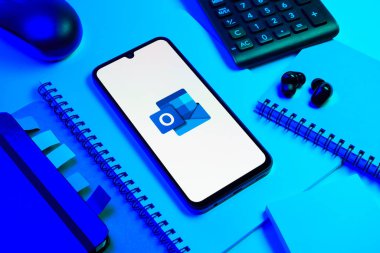 Prag, Çek Cumhuriyeti - 08 18 2025: Merkezde Outlook logosunu gösteren bir cep telefonu ile ofis malzemeleri düzenlemesi. Outlook iletileri göndermek ve yönetmek için bir e- posta platformudur.
