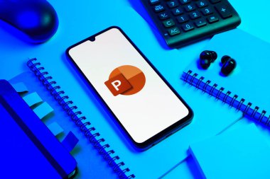 Prag, Çek Cumhuriyeti - 08 18 2025: Merkezde Powerpoint logosunu gösteren bir cep telefonu ile ofis malzemeleri düzenlemesi. Powerpoint sunumlar ve slayt gösterileri oluşturmak için bir yazılımdır..
