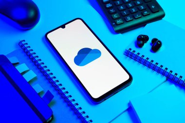 Prag, Çek Cumhuriyeti - 08 18 2025: Merkezde OneDrive logosunu gösteren bir cep telefonu ile ofis malzemeleri düzenlemesi. OneDrive dosyaları kaydetmek ve paylaşmak için bir bulut depolama platformudur.