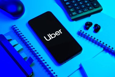 Prag, Çek Cumhuriyeti - 08 18 2025: Merkezde Uber logosu gösteren bir cep telefonu ile ofis malzemeleri düzenlemesi. Uber ulaşım ve dağıtım hizmetleri için bir gezinti selamlama uygulaması.
