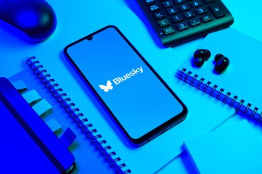Prag, Çek Cumhuriyeti - 08 18 2025: Merkezde Bluesky logosunu gösteren bir cep telefonu ile ofis malzemeleri düzenlemesi. Bluesky merkezi olmayan ağlar için bir sosyal medya platformudur..