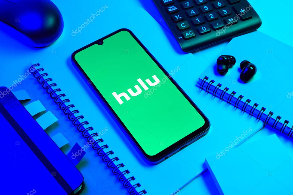 Prague, Czechia - 08 18 2025: An arrangement of office supplies with a mobile phone in the center displaying Hulu logo. Hulu is a streaming platform for TV shows, movies, and live TV.