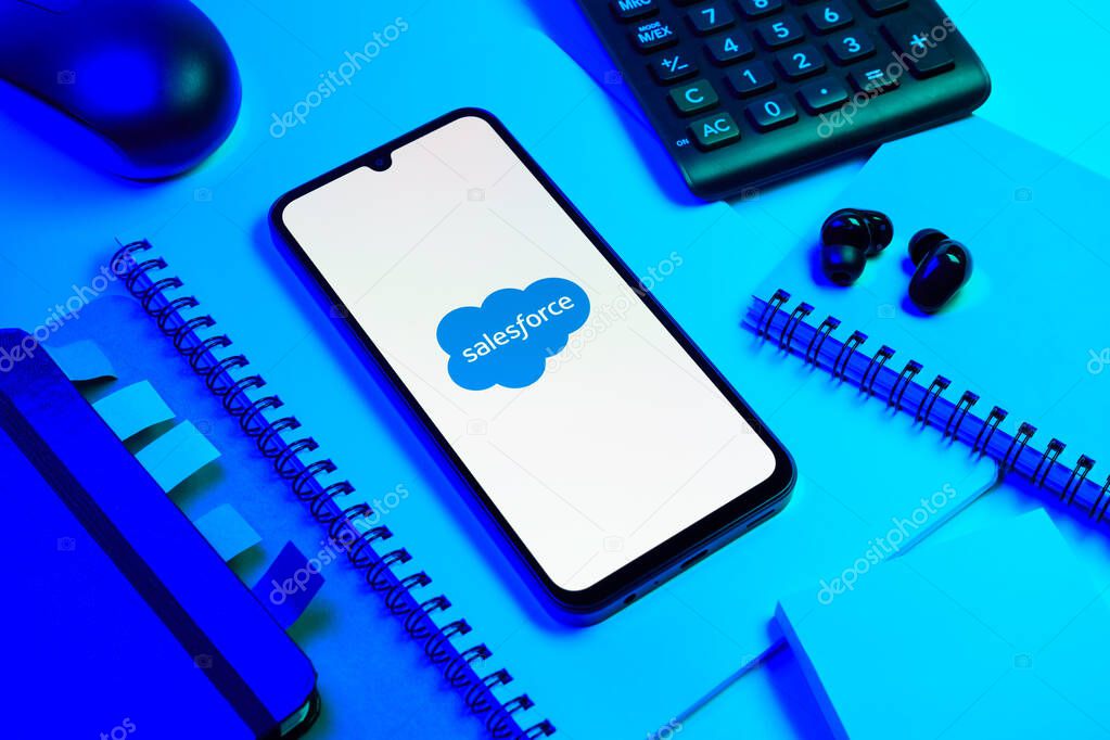 Prague, Czechia - 08 18 2025: An arrangement of office supplies with a mobile phone in the center displaying Salesforce logo. Salesforce is a platform for customer relationship management and cloud services.