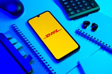 Prag, Çek Cumhuriyeti - 08 18 2025: Merkezde DHL logosu sergilenen bir cep telefonu ile ofis malzemeleri düzenlemesi. DHL uluslararası nakliye hizmeti sunan bir lojistik şirketidir..