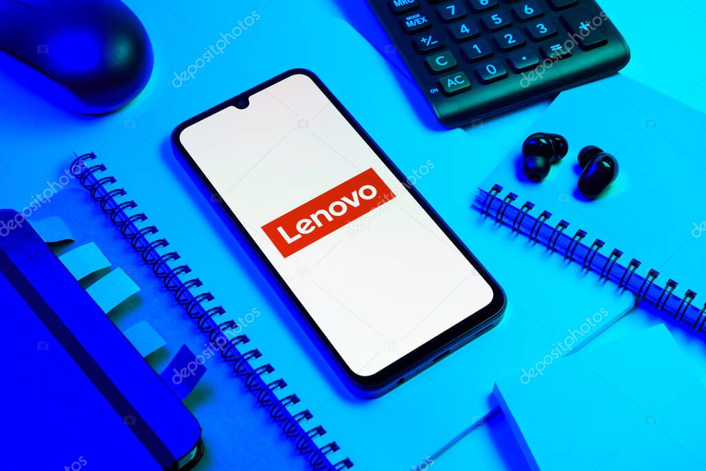 Prague, Czechia - 08 18 2025: An arrangement of office supplies with a mobile phone in the center displaying Lenovo logo. Lenovo is a technology company producing computers and electronics.