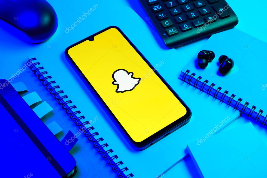 Prague, Czechia - 08 18 2025: An arrangement of office supplies with a mobile phone in the center displaying Snapchat logo. Snapchat is an app for sending photos, videos, and temporary messages.