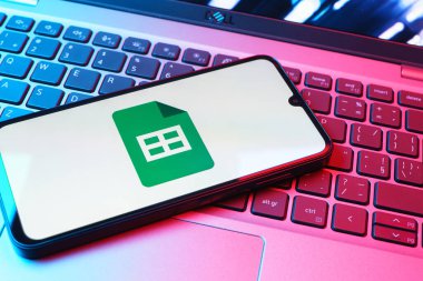 Prag, Çek Cumhuriyeti - 08 01 2025: Laptop klavyesinde duran bir cep telefonu Google Sheets logosunu görüntüler. Google Sayfalar tablo oluşturmak ve yönetmek için bir platformdur.