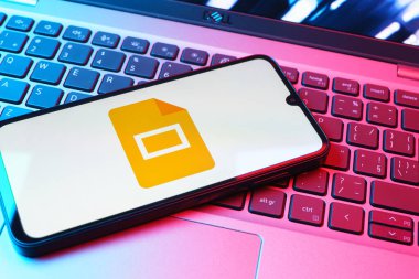 Prag, Çek Cumhuriyeti - 08 01 2025: Laptop klavyesinde duran bir cep telefonu Google Slides logosunu görüntüler. Google Slides sunumlar ve slayt gösterileri oluşturmak için bir platformdur.