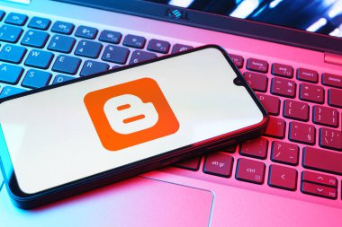 Prag, Çek Cumhuriyeti - 08 01 2025: Dizüstü bilgisayarın üzerinde duran bir cep telefonu Blogger logosunu gösterir. Blogger blog oluşturma ve yayınlama için bir platformdur.