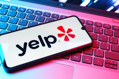 Prag, Çek Cumhuriyeti - 08 01 2025: Laptop klavyesinde duran bir cep telefonu Yelp logosunu gösterir. Yelp yerel işletmeleri bulmak ve incelemek için bir platformdur.