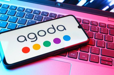 Prag, Çek Cumhuriyeti - 08 01 2025: Dizüstü bilgisayarın üzerinde duran bir cep telefonu Agoda logosunu gösteriyor. Agoda, otelleri ve seyahat yerlerini ayırtmak için bir platform..