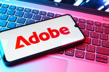 Prag, Çek Cumhuriyeti - 08 01 2025: Dizüstü bilgisayarın üzerinde duran bir cep telefonu Adobe logosunu gösterir. Adobe yaratıcı araçlar ve hizmetler sunan bir yazılım şirketidir..