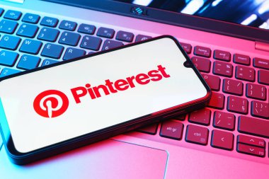 Prag, Çek Cumhuriyeti - 08 01 2025: Dizüstü bilgisayarın üzerinde duran bir cep telefonu Pinterest logosunu gösteriyor. Pinterest fikirleri görsel olarak keşfetmek ve kaydetmek için bir platformdur..