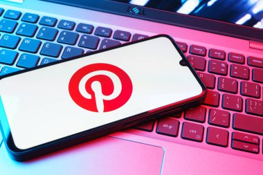 Prag, Çek Cumhuriyeti - 08 01 2025: Dizüstü bilgisayarın üzerinde duran bir cep telefonu Pinterest logosunu gösteriyor. Pinterest fikirleri görsel olarak keşfetmek ve kaydetmek için bir platformdur..