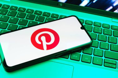 Prag, Çek Cumhuriyeti - 08 01 2025: Dizüstü bilgisayarın üzerinde duran bir cep telefonu Pinterest logosunu gösteriyor. Pinterest fikirleri görsel olarak keşfetmek ve kaydetmek için bir platformdur..
