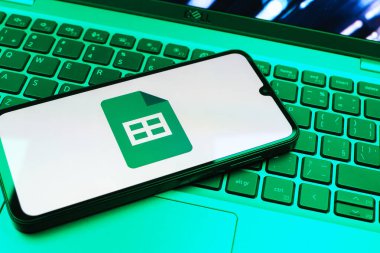 Prag, Çek Cumhuriyeti - 08 01 2025: Laptop klavyesinde duran bir cep telefonu Google Sheets logosunu görüntüler. Google Sayfalar tablo oluşturmak ve yönetmek için bir platformdur.