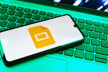 Prag, Çek Cumhuriyeti - 08 01 2025: Laptop klavyesinde duran bir cep telefonu Google Slides logosunu görüntüler. Google Slides sunumlar ve slayt gösterileri oluşturmak için bir platformdur.