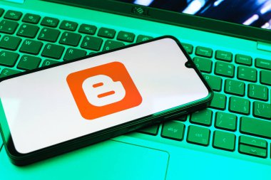 Prag, Çek Cumhuriyeti - 08 01 2025: Dizüstü bilgisayarın üzerinde duran bir cep telefonu Blogger logosunu gösterir. Blogger blog oluşturma ve yayınlama için bir platformdur.