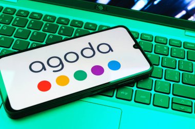 Prag, Çek Cumhuriyeti - 08 01 2025: Dizüstü bilgisayarın üzerinde duran bir cep telefonu Agoda logosunu gösteriyor. Agoda, otelleri ve seyahat yerlerini ayırtmak için bir platform..