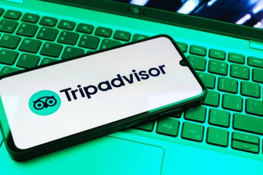 Prag, Çek Cumhuriyeti - 08 01 2025: Dizüstü bilgisayarın üzerinde bulunan bir cep telefonu TripDanışman logosunu gösteriyor. Seyahat danışmanı seyahat değerlendirmeleri, rezervasyonlar ve tavsiyeler için bir platformdur..