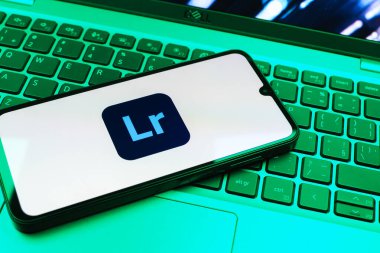 Prag, Çek Cumhuriyeti - 08 01 2025: Dizüstü bilgisayarın üzerinde duran bir cep telefonu Lightroom logosunu gösteriyor. Lightroom fotoğraf düzenleme ve yönetim için bir yazılımdır..