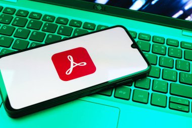 Prag, Çek Cumhuriyeti - 08 01 2025: Dizüstü bilgisayarın üzerinde duran bir cep telefonu Acrobat Reader logosunu gösteriyor. Acrobat Reader, PDF belgelerini görüntülemek ve yönetmek için bir platformdur.