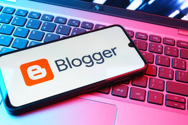 Prag, Çek Cumhuriyeti - 08 01 2025: Dizüstü bilgisayarın üzerinde duran bir cep telefonu Blogger logosunu gösterir. Blogger blog oluşturma ve yayınlama için bir platformdur.
