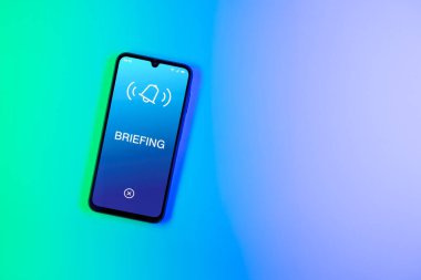 Arka plandaki telefon Brifing metnini görüntüler. Brifing, görevler hakkında kısa bir toplantı veya güncellemedir.