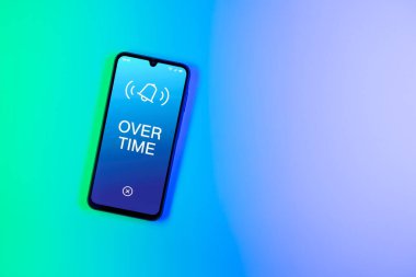 Arka plandaki telefon Fazla mesai metnini görüntüler. Fazla mesai normal çalışma saatlerinin ötesinde yapılır..