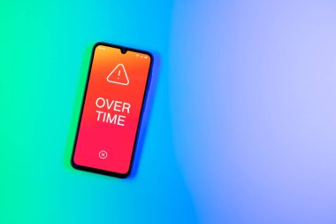 Arka plandaki telefon Fazla mesai metnini görüntüler. Fazla mesai normal çalışma saatlerinin ötesinde yapılır..