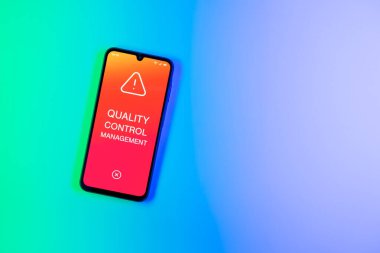 Arka plandaki telefon Kalite Kontrol Yönetimi metnini görüntüler. Kalite Kontrol Yönetimi ürün veya hizmetlerin standartları karşılamasını sağlıyor.