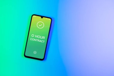 Arka plandaki telefon O Hour sözleşmesi metnini görüntüler. O Saat Sözleşmesi garantili çalışma saatleri olmayan bir sözleşmedir..