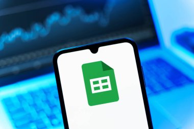 Prag, Çek Cumhuriyeti - 08 12 2025: Bir dizüstü bilgisayarın önünde duran bir cep telefonu Google Sheets logosunu görüntüler. Google Sayfalar tablo oluşturmak ve yönetmek için bir platformdur.