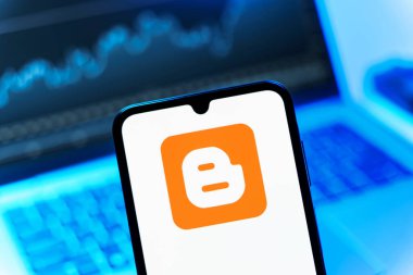 Prag, Çek Cumhuriyeti - 08 12 2025: Bir dizüstü bilgisayarın önünde duran bir cep telefonu Blogger logosunu görüntüler. Blogger blog oluşturma ve yayınlama için bir platformdur.