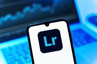 Prag, Çek Cumhuriyeti - 08 12 2025: Dizüstü bilgisayarın önünde duran bir cep telefonu Lightroom logosunu gösteriyor. Lightroom fotoğraf düzenleme ve yönetim için bir yazılımdır..
