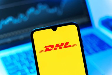 Prag, Çek Cumhuriyeti - 08 12 2025: Bilgisayarın önünde duran bir cep telefonu DHL logosunu gösteriyor. DHL uluslararası nakliye hizmeti sunan bir lojistik şirketidir..