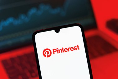 Prag, Çek Cumhuriyeti - 08 12 2025: Bilgisayarın önünde duran bir cep telefonu Pinterest logosunu gösteriyor. Pinterest fikirleri görsel olarak keşfetmek ve kaydetmek için bir platformdur..