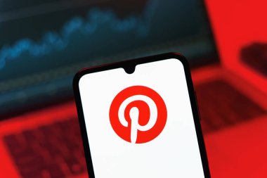 Prag, Çek Cumhuriyeti - 08 12 2025: Bilgisayarın önünde duran bir cep telefonu Pinterest logosunu gösteriyor. Pinterest fikirleri görsel olarak keşfetmek ve kaydetmek için bir platformdur..