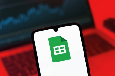 Prag, Çek Cumhuriyeti - 08 12 2025: Bir dizüstü bilgisayarın önünde duran bir cep telefonu Google Sheets logosunu görüntüler. Google Sayfalar tablo oluşturmak ve yönetmek için bir platformdur.