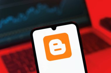 Prag, Çek Cumhuriyeti - 08 12 2025: Bir dizüstü bilgisayarın önünde duran bir cep telefonu Blogger logosunu görüntüler. Blogger blog oluşturma ve yayınlama için bir platformdur.