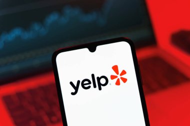 Prag, Çek Cumhuriyeti - 08 12 2025: Laptopun önünde duran bir cep telefonu Yelp logosunu gösteriyor. Yelp yerel işletmeleri bulmak ve incelemek için bir platformdur.